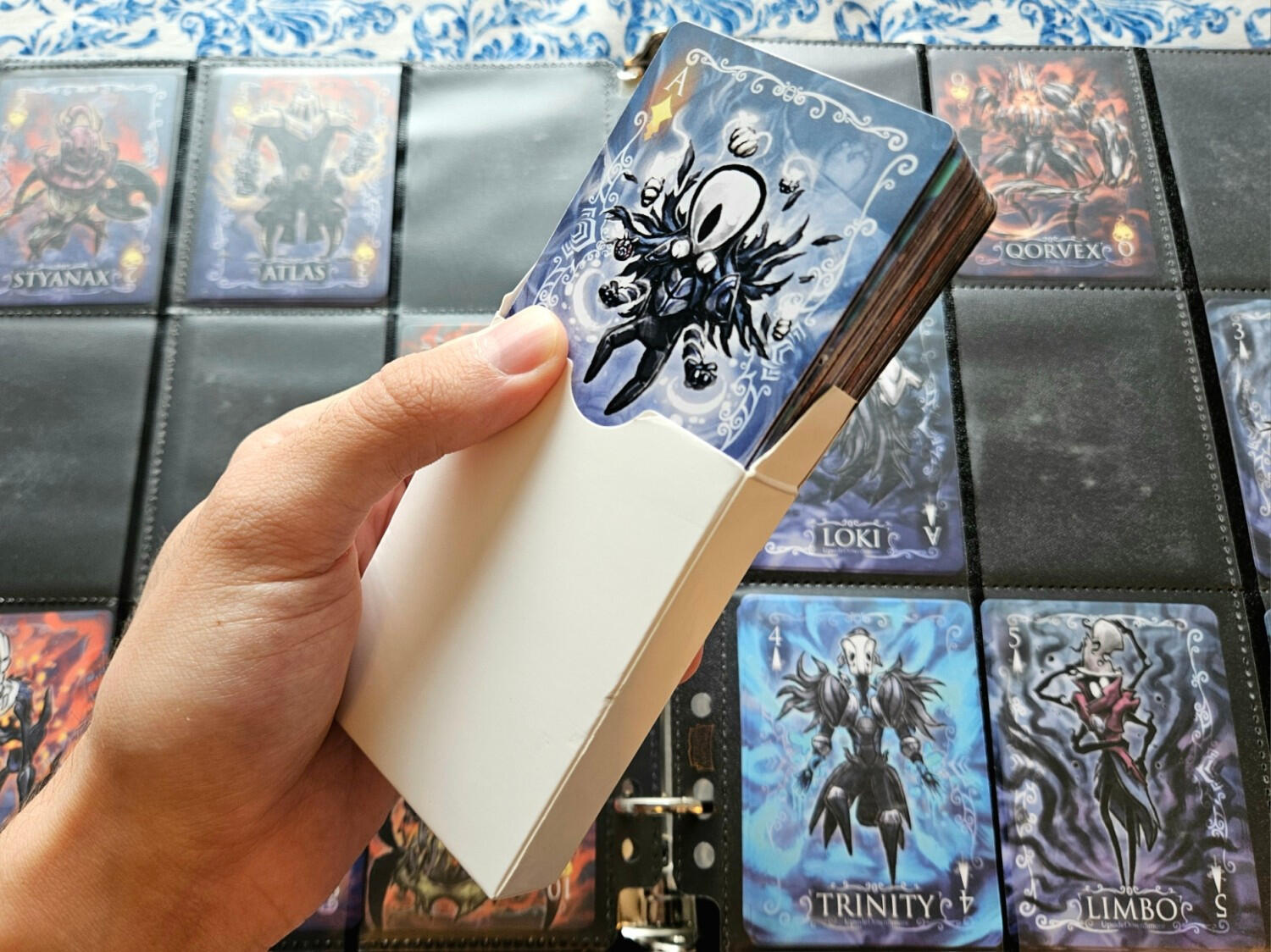 Photo of a deck of custom-made Hollowframe playing cards in my hand, in front of a partially-filled binder of some of the cards slotted in.